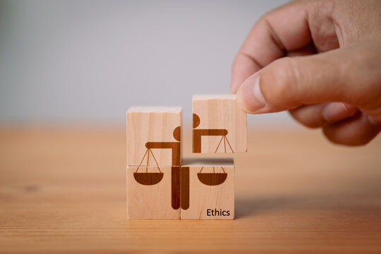 Concept of business ethics and moral principles, as a hand holds wooden cubes with "ETHICS" symbols. This emphasizes the importance of business integrity, good governance policies and ethical