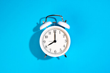 White alarm clock on a blue background isolated, top view.