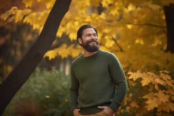 Handsome bearded man in green sweater posing in autumn park.