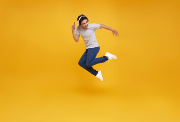 Fototapeta na wymiar Cool young asian man jumping isolated on yellow background studio portrait. Listening music with headphones, dancing. People lifestyle concept.