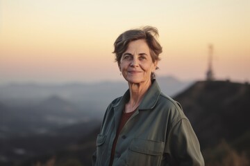 Portrait of a smiling senior woman on top of a mountain at sunset