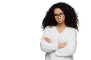 Self confident dark skinned ethnic female keeps hands crossed over chest, looks seriously at camera, wears optical spectacles and white sweater, stands against grey background with empty space