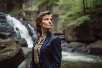 Portrait of a beautiful young woman in a blue suit standing in front of a waterfall.