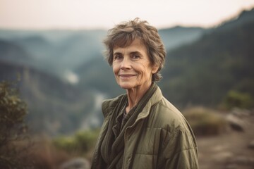 Portrait of smiling senior woman standing on top of mountain and looking at camera
