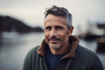 Obraz premium Portrait of handsome mature man with grey hair and beard looking at camera with smile while standing on pier