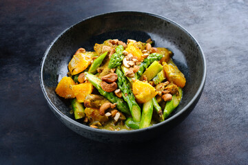 Traditional curry chicken fillet with orange, green asparagus and nuts in sweet sour vinaigrette served as a close-up in a design plate with text space
