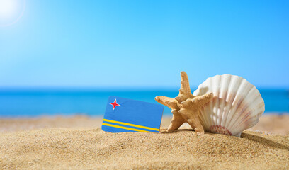 Tropical beach with seashells and Aruba flag. The concept of a paradise vacation on the beaches of Aruba