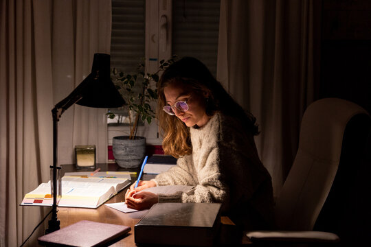 Young teenage girl student studying late at night in her room under the light of a lamp