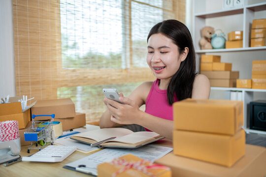 Woman uses a mobile phone to chat with customers who come to order product, Freelance work at home, Packaging on background, Sell online, Small business owner, Online shopping SME entrepreneur.