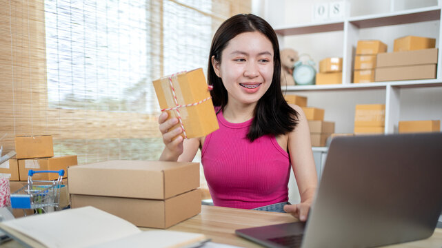 Woman uses a laptop to chat with customers who come to order product, Freelance work at home, Packaging on background, Sell online, Small business owner, Online shopping SME entrepreneur.