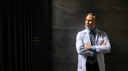 Hight contrast and drama concept. Portrait caucasian senior man doctor posing and arms crossed  at wellness center and hospital. healthcare and medicine