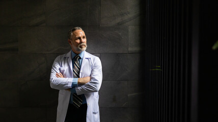 Hight contrast and drama concept. Portrait caucasian senior man doctor posing and arms crossed  at wellness center and hospital. healthcare and medicine