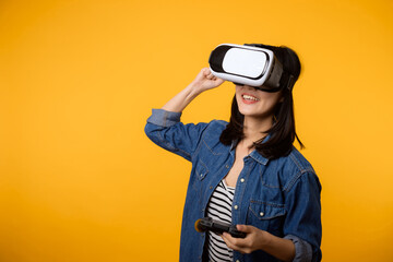 Young asian woman happy success wearing virtual reality headset game entertainment and holding joystick controller isolated on yellow background. Winner of cyber future video game concept.