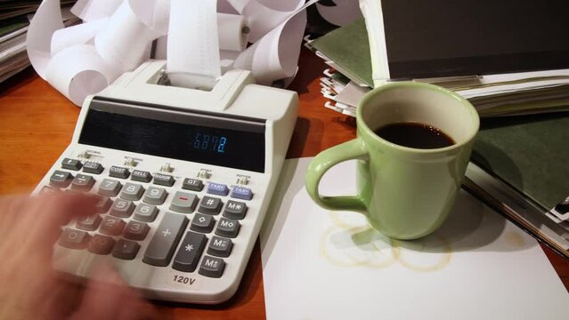 Time lapse of a man's hand using a calculator on a cluttered office desk.