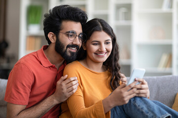 Happy Young Indian Couple Watching Videos On Smartphone At Home Together