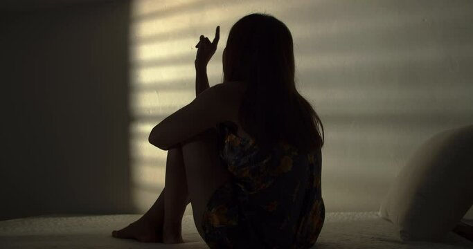 A lonely woman is sitting on the bed in a narrow dark room. This concept use for symptoms of stress, major depressive disorder (MDD), psychotic symptoms.