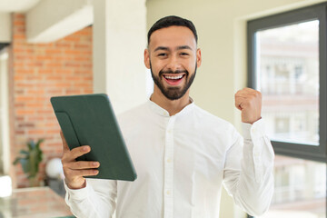 young  adult man feeling shocked,laughing and celebrating success. touchscreen pad  concept