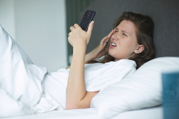 Girl with vision problems tries to read text on the phone. Bad vision concept. Woman looking at the screen of a mobile phone, having vision problems. selective focus in bed in bedroom in the morning  - obrazy, fototapety, plakaty