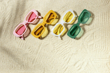 Fototapeta na wymiar Set of colorful sunglasses on beach sand background at sunlight, palm shadow. Summer fashion eyeglasses with colored glass. Summer vacation, summer rest concept. Minimal style flat lay, above view