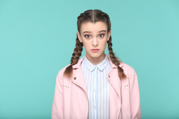 Fototapeta premium Portrait of shocked surprised teenager girl with braids wearing pink jacket looking at camera with big eyes, being astonished. Indoor studio shot isolated on green background.