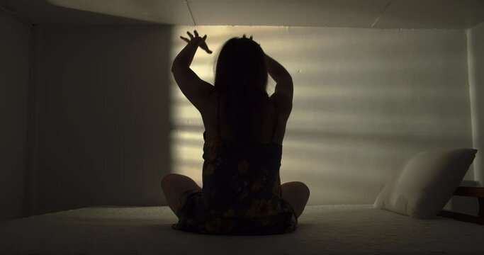 A lonely woman is sitting on the bed in a narrow dark room. This concept use for symptoms of stress, major depressive disorder (MDD), psychotic symptoms.