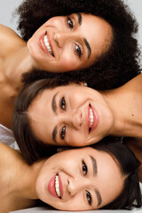 Young three diverse women with perfect glowing face skin posing together and smiling, vertical...