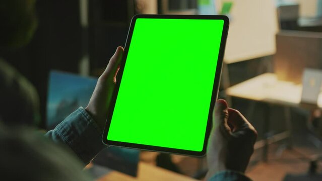 Footage of male hands holding digital tablet with green screen. Unrecognizable man scrolling news on blurred background of apartment. Evening. Indoors