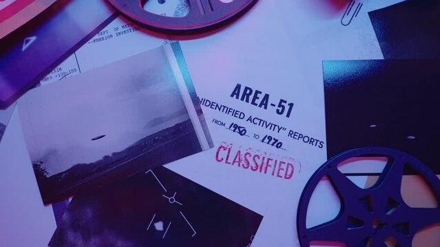 Top shot of various top secret classified documents reels and photographs of UFO. Reports and government papers relating to Area 51 and unidentified activity in retro looking official desk