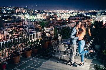 Couple at night, city lights view. Romantic date or proposal. Man and woman kiss and embrace on...