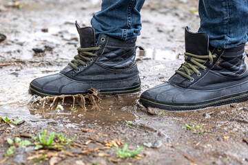 A man in jeans and boots walks through the swamp in rainy weather.