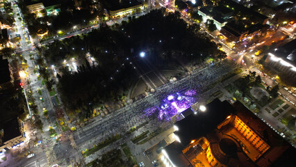 Top view from a drone of a big concert in the night city. Lots of people, rays of light. A large...