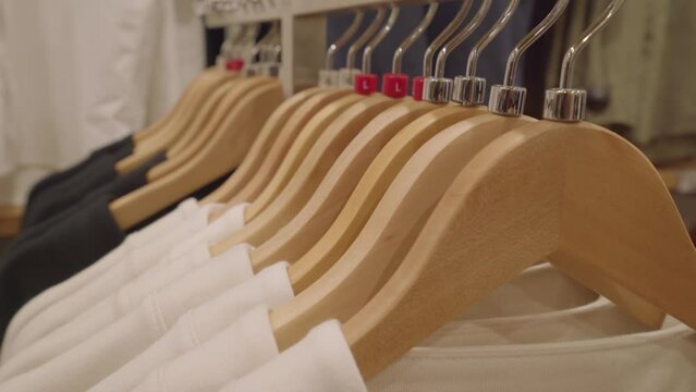 Close-up of a clothes hanger with a size icon in a fashion boutique clothing store. Sweatshirts hang on wooden hangers on a metal rack shelving 4K
