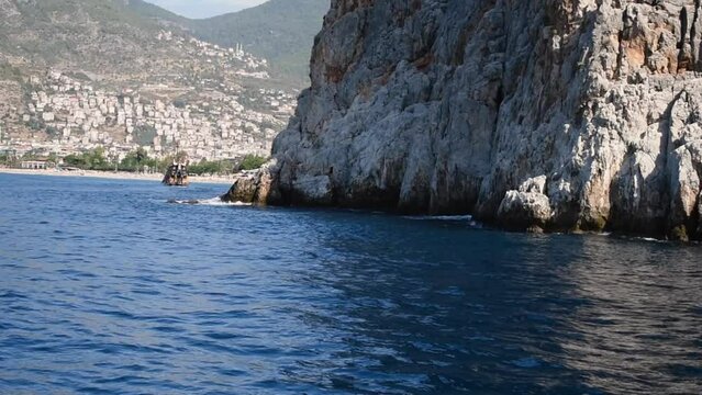 Movement on the Mediterranean Sea around the Dil Varna Burnu in the background of the coastline of Alanya, Turkey. Video 12 seconds. Blue waves wash over the stone rocky cliff of the promontorium