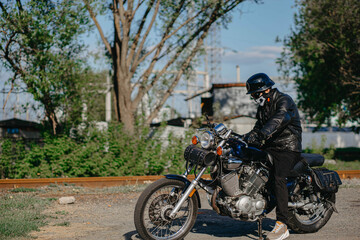 Fototapeta na wymiar stylish male motorcyclist biker in mask and helmet with custom handmade motorcycle cruiser chopper. Stylish retro motorcycle