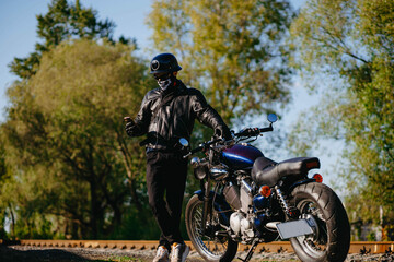 Obraz na płótnie Canvas stylish male motorcyclist biker in mask and helmet with custom handmade motorcycle cruiser chopper. Stylish retro motorcycle