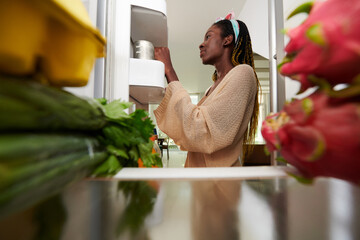 Young woman taking canned food out of fridge to cook dinner