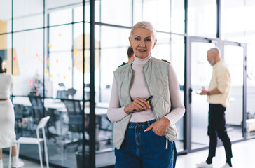 Fototapeta na wymiar Half length portrait of experienced female proud CEO in smart casual clothes looking at camera during working time in office interior, Caucasian financial expert 40s posing in coworking space