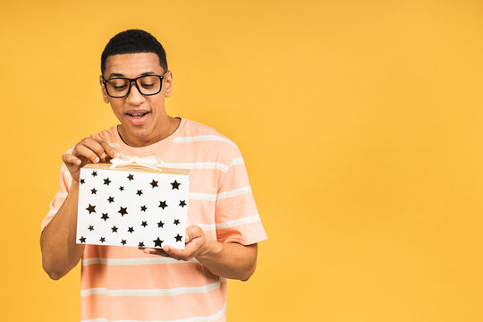Cheerful smiling african american man holding wrapped present box. Happy young man congratulating, giving birthday gift, isolated on yellow background.