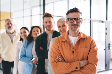 Half length of confident male entrepreneur in optical eyewear looking at camera during gather meeting for involved team brainstorming, portrait of Caucasian businessman in eyeglasses posing indoors - obrazy, fototapety, plakaty