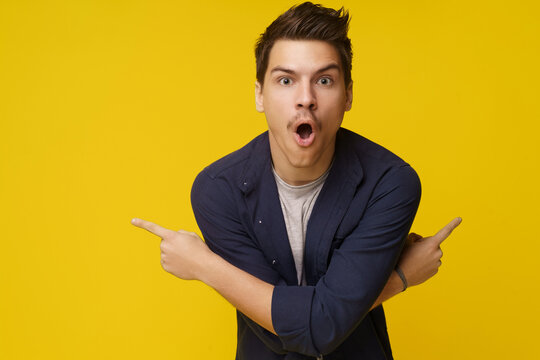 Surprised young man is depicted pointing with two crossed hands in opposite directions against yellow background, with plenty of copy space for text. Sense of astonishment, amazement, or shock, with