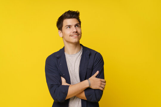 Young man in contemplative pose, with his hands crossed and eyes closed, lost in thought and dreaming of his future. Shot against a bright yellow background, the image conveys sense of optimism and