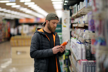 A bearded caucasian man customer is interested in a deodorant spray bottle at the grocery store, supermarket - obrazy, fototapety, plakaty