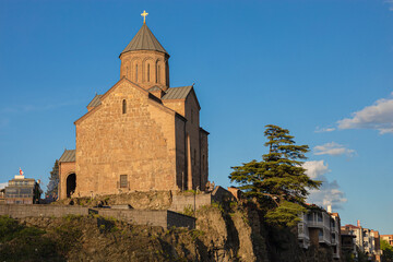 Fototapeta na wymiar Metekhi Christian Orthodox church on a cliff next to the Kura river during the golden hour