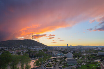 Tbilisi panorama at spectacular sunset, the Kura river reflects the colors of the sunset, bright beautiful orange clouds over the city.