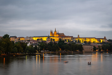 Naklejka premium Illuminated Castle of Prague and Saint Vitus Cathedral as seen from the shore of the Vltava river at dusk. Long exposure.