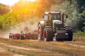 Modern agricultural  tractor is cultivating farm land after wheat harvest.Green tractor works the land.Harvest season