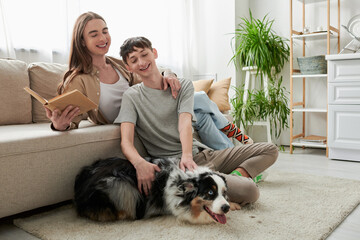 cheerful gay man sitting on carpet and cuddling Australian shepherd dog young partner with long...