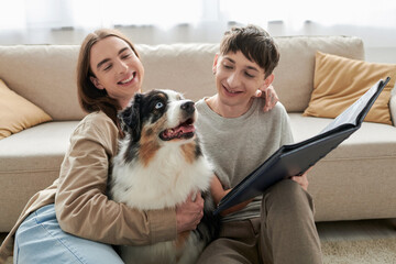 smiling and young gay men looking together at Australian shepherd dog and holding photo album while...