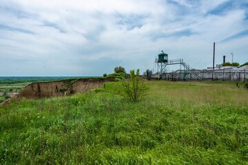 A bare clay slope of a ravine near an abandoned prison for criminals with a watchtower on a grassy plain in southern Russia on a sunny spring day.