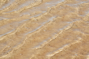 Close-up of a sea wave with white foam flowing on a pebble beach. Background with crystal clear water and sea rocks on the theme of seaside holidays and family weekends on the beach.
